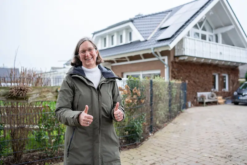 Zufriedene Kundin vor ihrem Haus mit neuem Dach und Photovoltaik