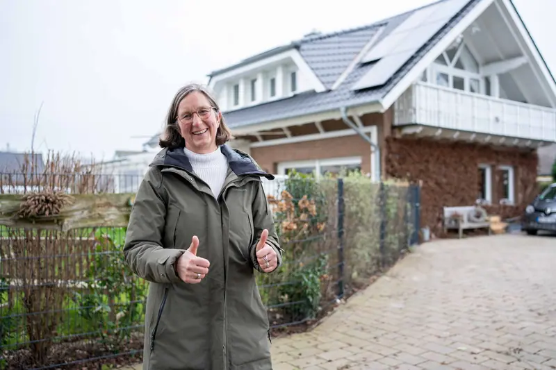 Zufriedene Kundin vor ihrem Haus mit neuem Dach und Photovoltaik