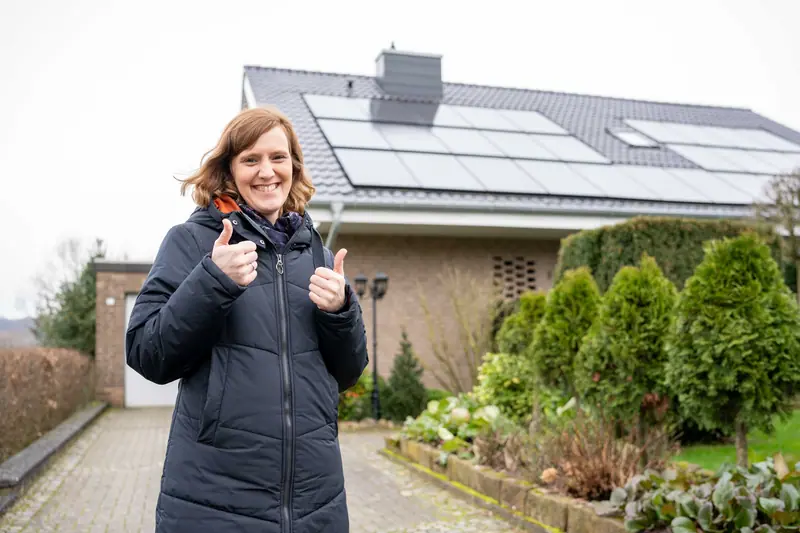 Zufriedene Kundin vor ihrem Haus mit neuem Dach und Photovoltaikanlage