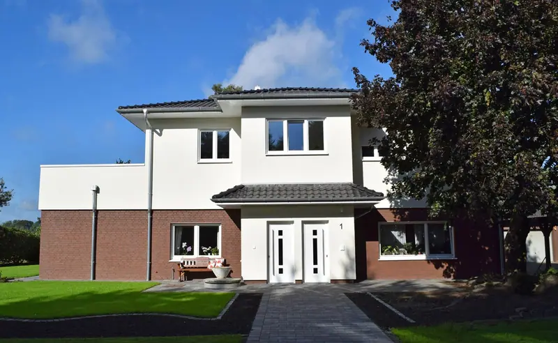 Zweigeschossiges Haus mit weißem Putz und Klinkersockel